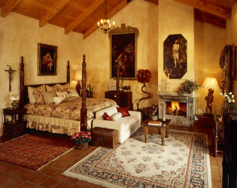 Dormitorio principal con cama de columnas en madera tallada. Se destacan el baúl colonial incrustado con motivos geométricos, tres óleos coloniales, un atril de plata martillada y, a la derecha de la chimenea, con elementos de piedra originales incorporados, una lámpara italiana de madera tallada, que representa a dos niños.