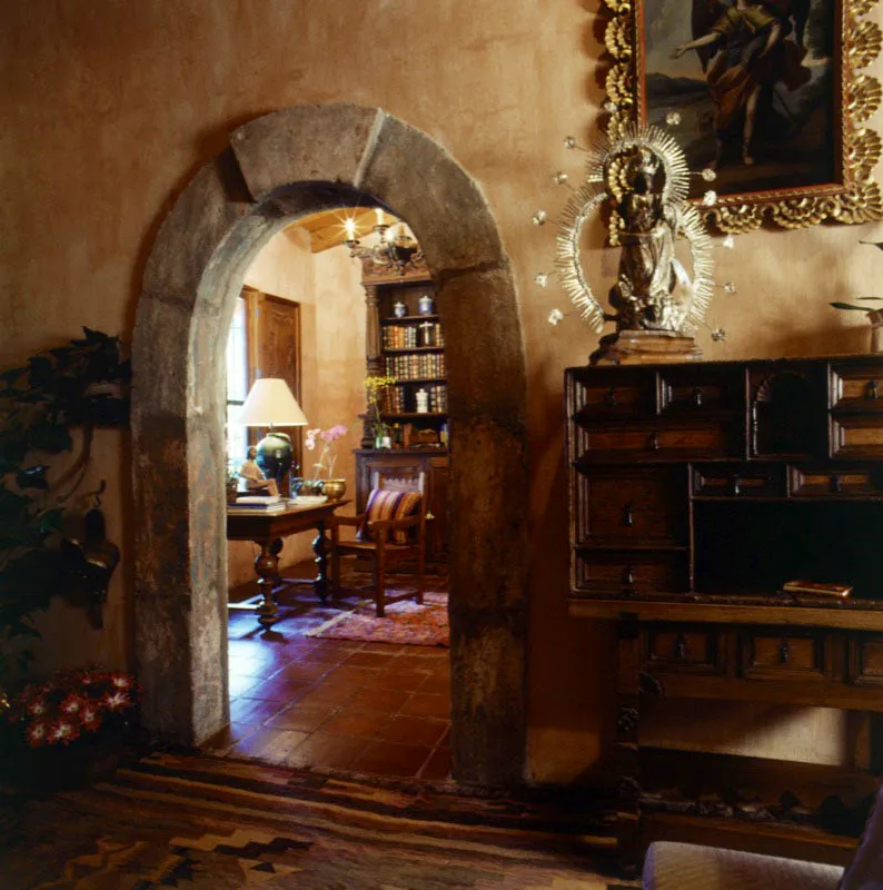 Entrada al escritorio, que posee una hermosa biblioteca en madera tallada, a través de un arco de piedra colonial incorporado. En primer plano, una Virgen de Concepción en madera tallada y policromada, con resplandor de plata, sobre un bargueño colonial.