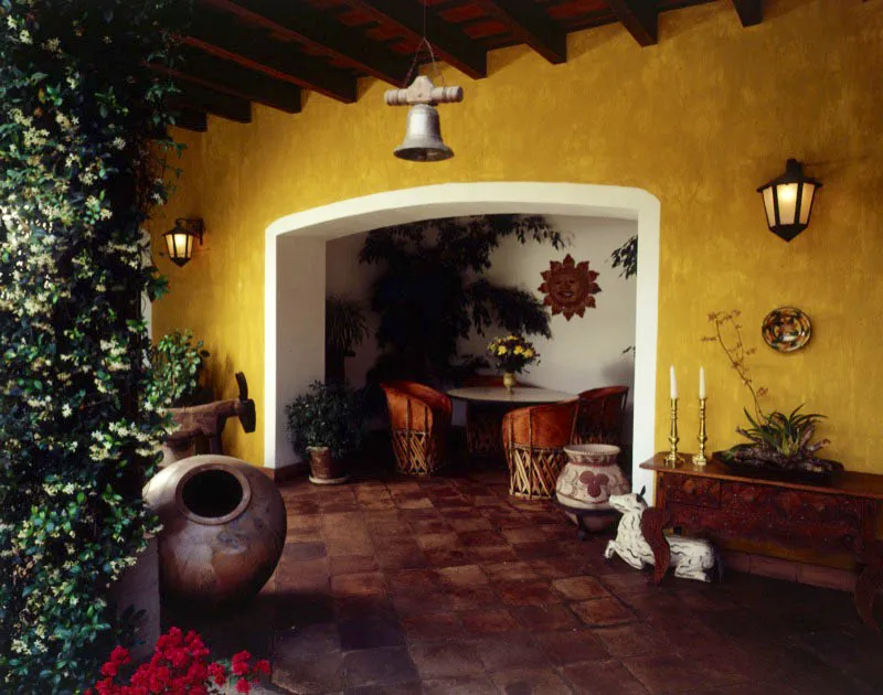 Rincón comedor integrado a un patio en una casa restaurada de Antigua, con mesa de hierro forjado y sillas equipales mexicanas en cuero de cerdo.A la derecha, mesa primitiva de Nahualá con candeleros de bronce. El piso es de baldosa
de barro de la zona y en él reposan diferentes animales en madera de talla popular guatemalteca.