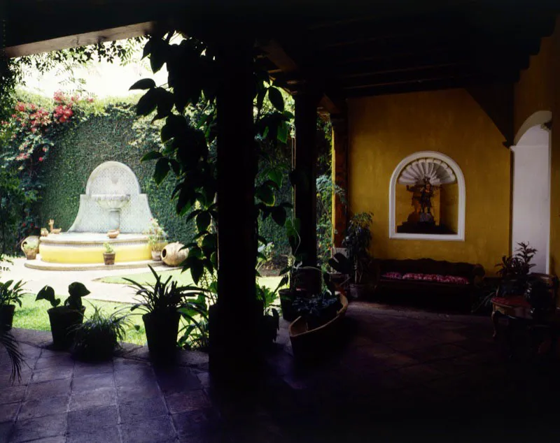 Al fondo de este patio, una pila contemporánea al estilo tradicional forrada en azulejos, rodeada de un jardín al que se abren los corredores de la casa. A la derecha, nicho decorado en yeso con forma de resplandor, que contiene un pequeño arcángel de madera tallada y policromada.