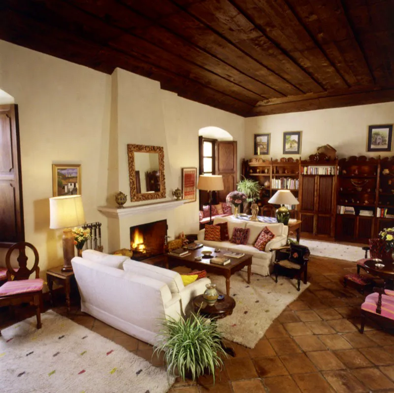 Salón principal de una casa restaurada antigüeña, centrado en la chimenea, con espejo contemporáneo de estilo barroco. Al fondo, una estantería de madera tallada en la que se exhiben piezas de cerámica precolombina maya.