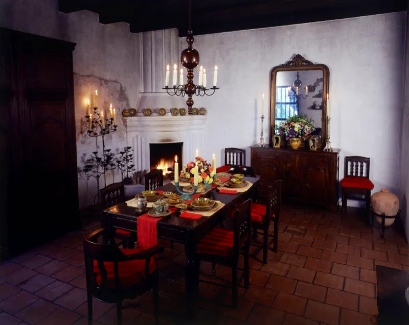 Comedor de la misma casa restaurada, con chimenea incorporada, piso de baldosa de barro y muebles de principios de siglo. A la izquierda, un armario grande de madera y varios candelabros de hierro forjado; al fondo, un trinchante con espejo dorado; sobre la mesa, arreglada con piezas de mayólica antigüeña, dos candelabros
de cerámica; del techo pende una araña de madera y hierro con velas.
