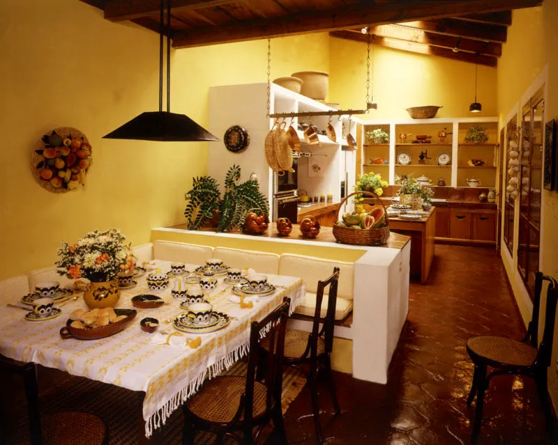 Desayunador y cocina de la misma casa. Sigue la predileccin por la lnea recta y los colores claros, que tambin se dan en el mantel de tela tpica de la mesa, con vajilla de cermica mexicana. En el muro de la izquierda, un arreglo de frutas de cermica pintada antigea. 