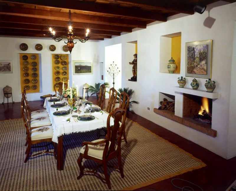 Comedor de la misma casa. Se continúa el juego de planos en los nichos cuadrados,
esta vez con fondo amarillo, en los que también se exhiben piezas artísticas (platos de mayólica antigüeña y española y una escultura popular) además de una chimenea igual a la del salón. En el centro, la mesa con mantel típico claro y platos de vidrio y mayólica, así como servilleteros de colibríes pintados, ejemplos de la nueva artesanía popular local. La alfombra de fibras de pita y algodón fue elaborada en Antigua.