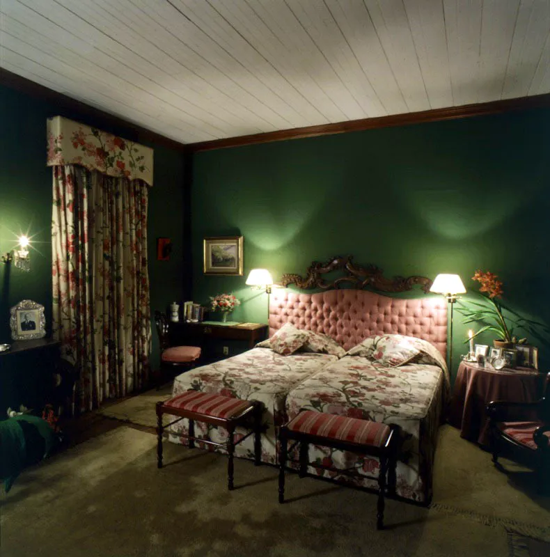 Dormitorio principal de la casa en Cobn, con la cabecera de la cama tapizada y una talla de madera barroca sobrepuesta al fondo verde del muro. 