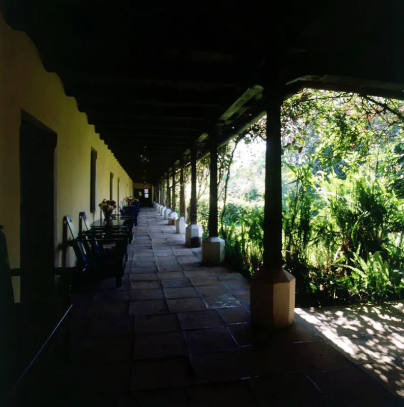 Casa cobanera, convertida hoy en el Hotel La Posada. A la izquierda, el largo corredor frente al jardín, con piso en grandes baldosas de terracota, columnas apoyadas en bases octogonales de cemento pintado, y muebles rústicos sencillos a lo largo del mismo.