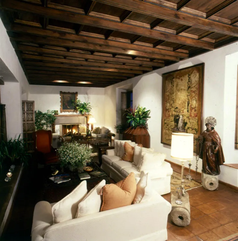 Salón principal de la misma casa. Al fondo, un óleo colonial de San José. A la derecha una escribanía antigua en madera, contra la pared un gobelino europeo y una gran talla en madera con aureola de plata. En el piso se aprecian bases coloniales de columnas en piedra utilizadas en forma de mesa. El artesonado le da carácter y calidez al espacio.