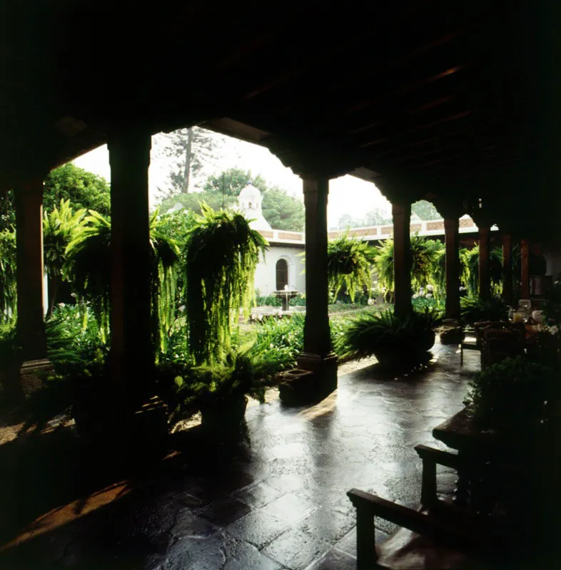 Patio principal de una casa restaurada en Antigua, que respeta la arquitectura tradicional. Se destaca la baldosa de barro encerada, las columnas y zapatas de madera, las colas de quetzal que cuelgan en la forma tradicional y la fuente de
piedra del patio.