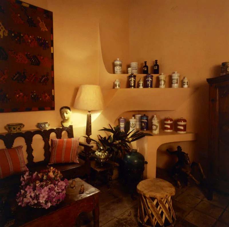 En el rincón del estudio de la casa, con mampostería pintada que sostiene una hermosa colección de pomos y recipientes de vidrio y cerámica de farmacia antigua, un gran textil guatemalteco enmarcado y una banca colonial en madera, con cojines en tela típica del país.