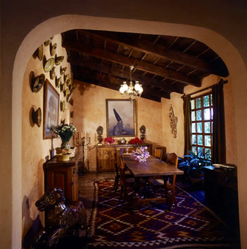 Vista del comedor de la misma casa. En el centro, una mesa rústica encerada; a la izquierda, un trinchante sobre el que reposa una buena selección de vasijas maya, y sobre la pared, una colección de platos de mayólica tradicional de Antigua. Al fondo, una pintura del artista mexicano Rafael Coronel, debajo de la cual hay otro trinchante tallado mexicano con dos floreros antiguos de latón. Complementan el ambiente un kilim turco de vivos colores en el piso, la techumbre de madera, un colocho antiguo en pan de oro al lado de la ventana y la lámpara eléctrica de quinqués.