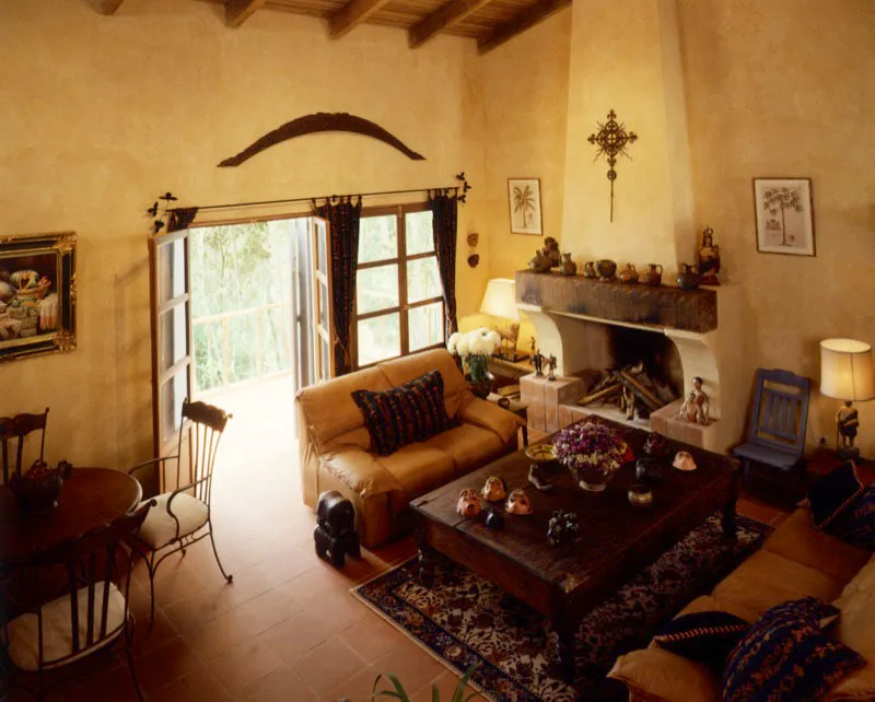 Estar del dormitorio de una de las casas que forman este complejo campestre. La distribución es similar: dos sillones y una mesa frente a la chimenea, también decorada con alfarería popular. En las paredes dos grabados y una cruz de hierro forjado.