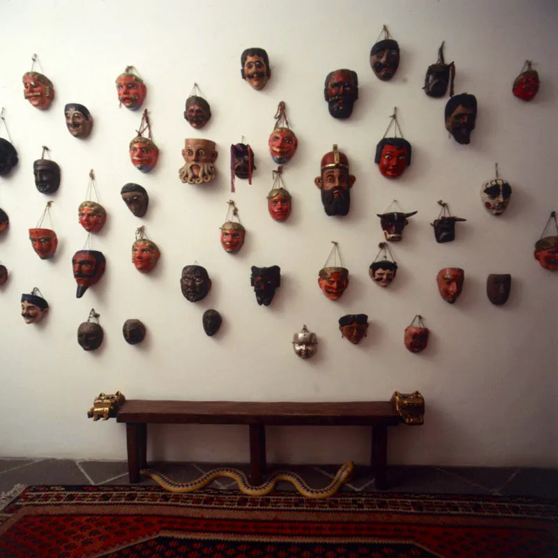 Otros detalles de la misma residencia. El muro blanco con una gran multitud de máscaras de diferentes danzas del altiplano guatemalteco, en las que puede apreciarse la amplia tipología que requieren los diversos bailes folclóricos: el de la Conquista, el de moros y cristianos, el del torito. Debajo, banca rústica tallada en madera con cabezas de jaguar doradas.