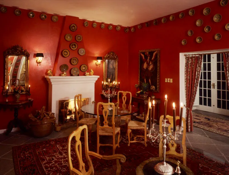 Comedor pintado de rojo profundo, que no impide exhibir en todo su valor la abundante colección de mayólica antigüeña y las pinturas coloniales. A la izquierda, la chimenea, a cuyos lados cuelgan dos espejos republicanos en pan de oro con sus correspondientes consolas de madera tallada debajo. Las dos mesas contemporáneas de vidrio se apoyan en morteros de madera rústica que descansan sobre una alfombra oriental también de tonos rojos. Sobre las mesas, unos candelabros de plata colonial guatemalteca.