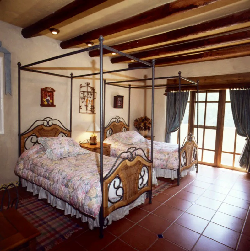 Dormitorio de una casa contemporánea a orillas del lago en Amatitlán, cerca de la ciudad de Guatemala, en el que se combinan la sencillez del piso de baldosa de barro, las camas de hierro forjado con mimbre, las vigas de madera del techo y los muros blancos, sobriamente decorados.