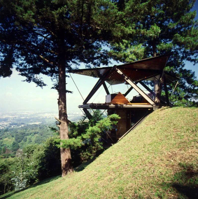 Aqu se aprecia la audaz colocacin de la casa sobre la ladera, con una extraordinaria vista del valle de la ciudad de Guatemala. Cuatro hojas se abren hacia arriba para formar las ventanas, e igual nmero hacia abajo, como terrazas voladizas. La casa cerrada tiene forma de octaedro y consta de dos niveles, sala, cocina y comedor en el piso superior, dos habitaciones, bao y escritorio en el inferior. Cerrada mide 36mt.2, abierta alcanza 112 mt.2. 