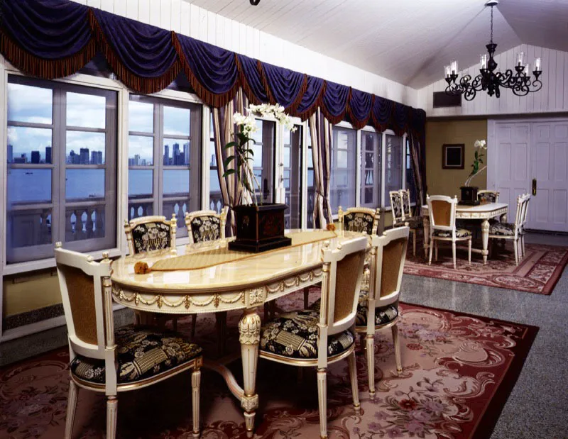 Comedor estilo Luis XVI, acabado en antique off white, con detalles en laminado de oro. Alfombras francesas. A través de los ventanales se aprecia la Bahía de Panamá y Punta Paitilla con sus altos edificios.