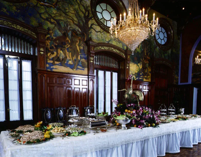 Vista norte del comedor, la mesa servida con viandas y adornada con flores y frutas tropicales.