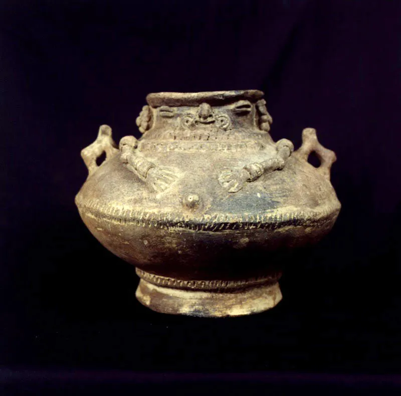 Cultura Chimila. Cántaro antropomorfo
Cerámica, 17,7 x 25 cm (diámetro)
Los grupos prehispánicos sedentarios que se ubicaron a lo largo del río Magdalena presentan cierta dificultad para su clasificación y caracterización por haber sido el río, precisamente, la ruta natural e ineludible para realizar los intercambios comerciales entre las diversas culturas.
Sin embargo, las urnas funerarias son el elemento arqueológico distintivo de la zona y se corresponden con las prácticas de enterramiento en grandes recipientes cerámicos, de forma cilíndrica, principalmente.
En este caso, la tapa de la urna aquí reproducida posee características chimila claras como el uso de orejeras. Definitoria de la tradición funeraria del Magdalena es la postura de las manos sobre el vientre, con los dedos extendidos aparentando hundirse en la piel. Este gesto, según Gerardo Reichel-Dolmatoff, es representativo del regreso del cadáver al útero materno.