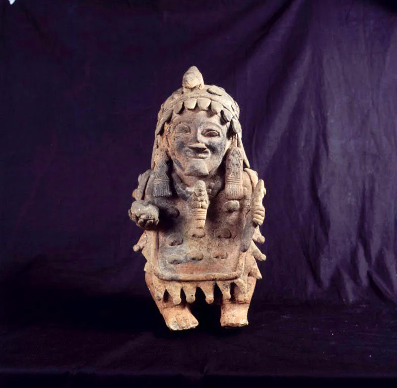 Cultura Jamacoaque. Figura antropomorfa.
27 x 15 x 12 cm
Ubicada al norte de Manabí, la cultura jamacoaque (1200 d. C.) comparte las características de la evolución ceramista de la costa pacífica del actual Ecuador. En ella es distinguible un deseo de retratar el mundo físico y mitológico de la comunidad con la mayor fidelidad posible. Este “naturalismo” difícilmente se conseguía a través de pigmentos, por ello la cerámica de jamacoaque es cerámica de incisión, para el caso de los atuendos, alhajas y facciones. Las figuras femeninas llevan, por lo general, falda larga y el pecho, adornado con collares, exhibe senos rotundos. En las figuras masculinas es notable la variedad de atuendos y tocados. El personaje aquí representado lleva en las manos los utensilios típicos del chamán, su vestimenta deja ver la importancia de la ceremonia que presidirá; los diseños geométricos de las orejeras, junto con la figurilla que pende de su cuello, representación de un dios, constituyen atributos mágicos.