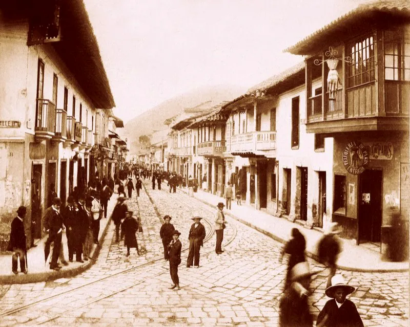 La Calle Real del Comercio comenzaba desde la calle 10 y se prolongaba hasta San Francisco. El tranvía de mulas partía del costado norte de la Plaza de Bolívar y seguía por la Calle Real. A la derecha se aprecia el balcón de esquina de la Casa del Florero. Foto de Henry Duperly, 1898.
