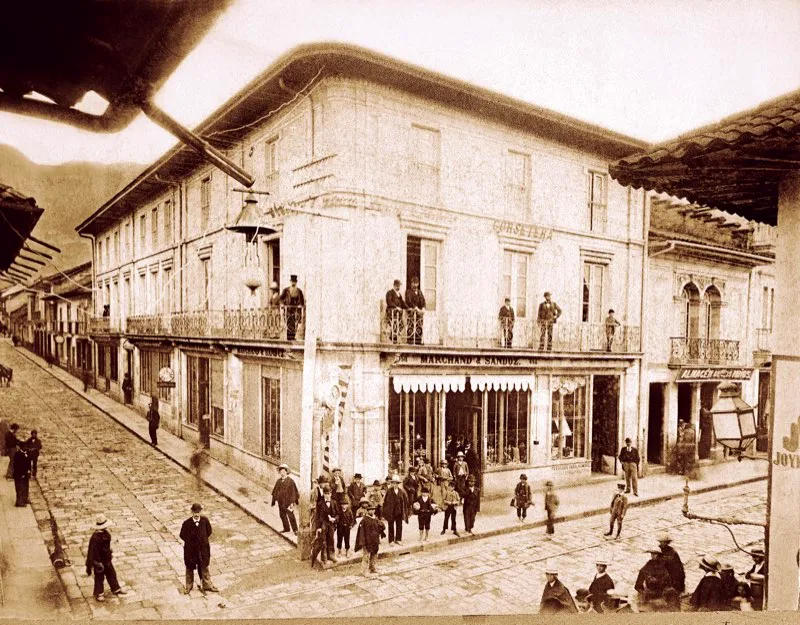 Alumbrado pblico elctrico de arco voltaico en la Segunda Calle Real, esquina de la carrera 7. con la calle 12. El sistema del arco voltaico tena muchas deficiencias y sola interrumpirse en las horas de ms congestin, entre las 6 de la tarde y las 8 de la noche, en que los bogotanos utilizaban el primitivo septimazo para tertuliar en las esquinas y pasar un rato agradable. En 1900 la Empresa de Energa Elctrica de los hermanos Samper Brush puso en funcionamiento la planta de El Charquito, primera hidroelctrica que suministr energa y fuerza motriz a Bogot y sustituy el obsoleto arco voltaico. Fotografa de Henry Duperly. 