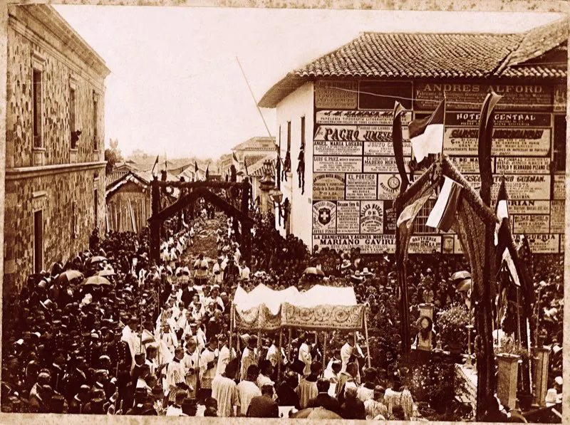 La profusión de carteles sobre el muro de la casa esquinera por la que está doblando la procesión del Corpus, que se efectuaba cada año en Bogotá desde los tiempos coloniales, y que en la foto corresponde al año de 1895, no ayuda a identificar el sitio. La procesión efectuaba un recorrido tradicional: partía de la Plaza de Bolívar, bajaba por la calle 15 (actual avenida Jiménez) al costado del Pasaje Rufino Cuervo (actual edificio Henry Faux) y regresaba por la carrera 8.a a la Plaza de Bolívar; pero en la gráfica no hay ningún punto de referencia que nos permita precisar con exactitud por dónde iba la procesión cuando se tomó la foto. Lo que sí se evidencia, en ésta como en las fotografías de las páginas inmediatamente anteriores, es que la lluvia no desalentaba el entusiasmo religioso de los bogotanos.