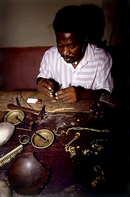 Taller de joyería de Emilio Cortés. Constituido por una mesa de trabajo, diferentes tipos de tenazas, pinzas, martillos, yunques, calabazos, estuches, frascos en donde reposan los metales preciados para la alquímica labor, y una balanza. En ella se pesa el oro luego de ser limpiado, después de efectuarse la aleación y, finalmente, al terminar la joya. La fragua está formada por una pequeña estufa que es avivada por un fuelle. Se usa para fundir el metal y para realizar, al final, el proceso del desborraje o dorado. Según la joya que se vaya a elaborar, la soldadura se hace con un soplete que permite ir encadenando, en secuencia, los hilos en oro o las uniones de las piezas. Barbacoas, Nariño. Diego Miguel Garcés