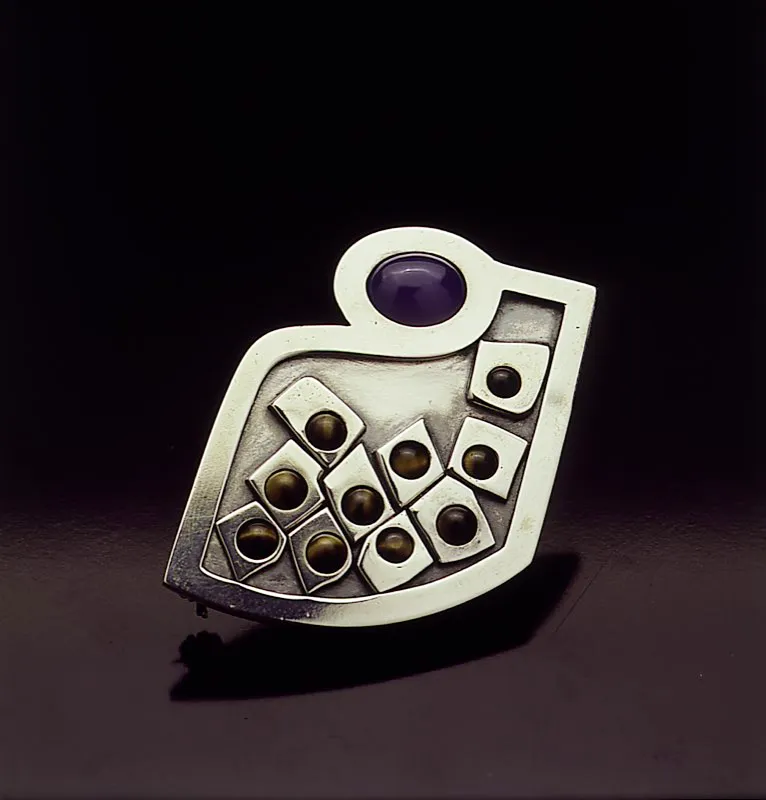 La joyería en Colombia continúa siendo una manifestación artística desarrollada con creatividad. El diseño está enriquecido con nuevos materiales e innovadoras ideas. Este broche de plata adornado con zircones y ojos de tigre, es un buen ejemplo de ello. Diseñado por J. A. Roda y elaborado por Nuri Carulla. Juan Camilo Segura