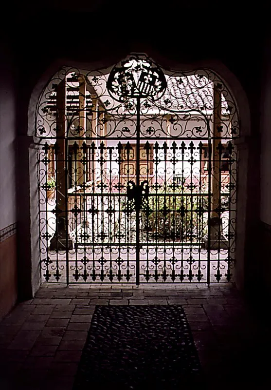 Puerta forjada en hierro, utilizada como divisin entre el zagun de acceso y el patio de una casa colonial. El desarrollo y dominio de las tcnicas del hierro permitieron durante la Colonia, particularmente en Momps y en Popayn, gran versatilidad en las diferentes aplicaciones de la metalrgica. Los descendientes de peninsulares, con ilustres abolengos, fueron anexando como un motivo ms a la ornamentacin, los escudos familiares de variados diseos. Siglo XVIII. Popayn, Cauca. Archivo Villegas Editores