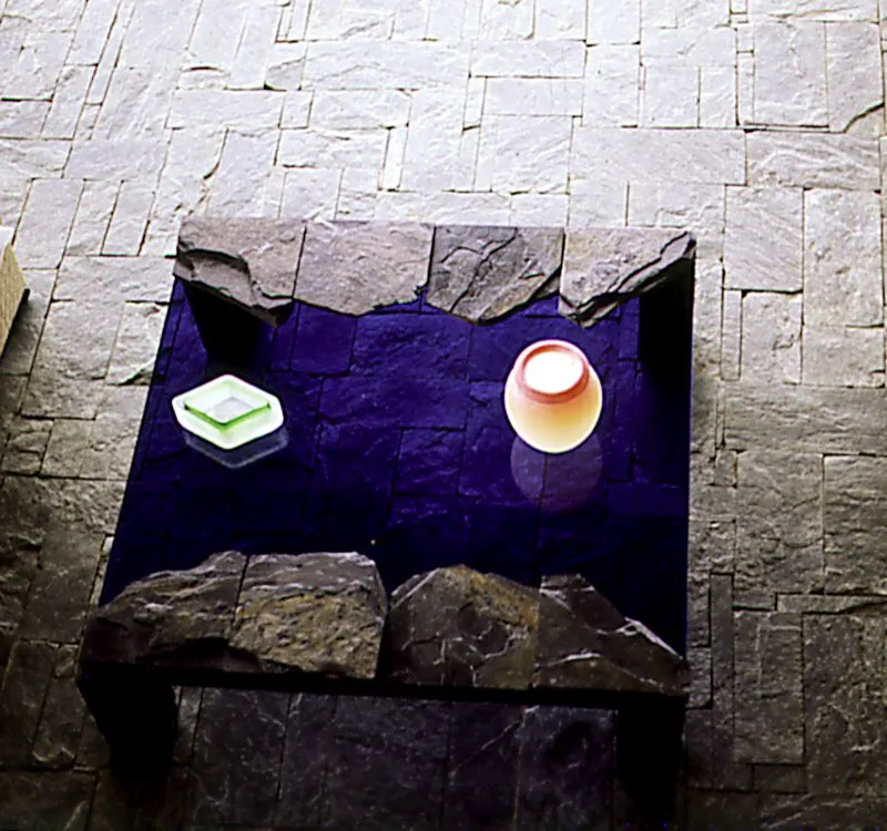 Mesa en cristal y lajas de piedra, ensambladas en dos de sus extremos. A través del vidrio se aprecia el piso, también en piedra, finamente trabajado. Hugo Zapata. Medellín, Antioquia. Simón Vélez