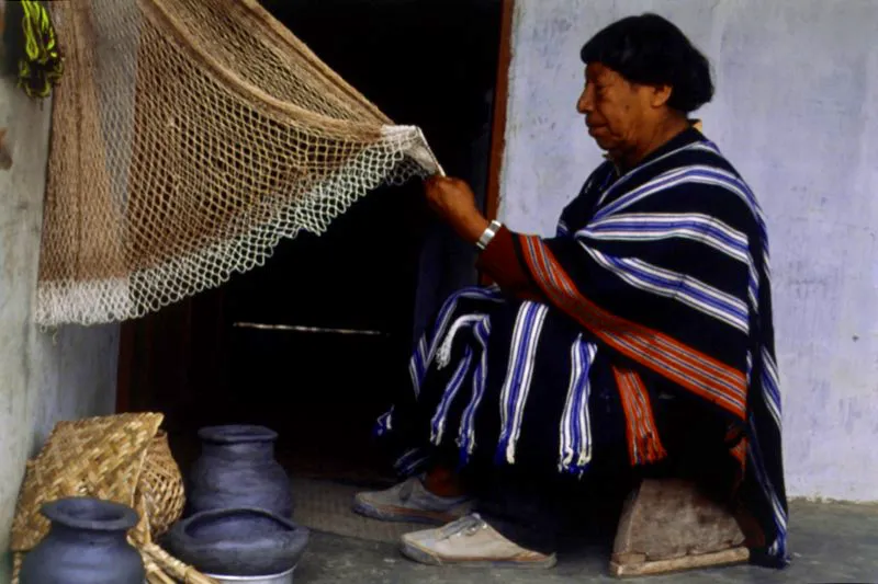 Alejo Agreda, cacique Kamsá, tejiendo una red. Viste un poncho característico, tejido en hilo sobre telar vertical. Los Kamsá viven en las montañas andinas que cruzan el valle de Sibundoy. La población actual es de cuatro mil, derivan su sustento de la agricultura, de la pesca y de la producción artesanal. San Francisco, Putumayo. Diego Miguel Garcés