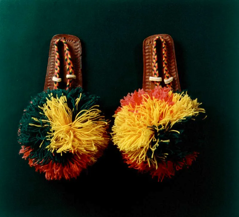 Guaireñas, sandalias guajiras tejidas en lana, sobre suela de cuero repujado. Prenda tradicional de las mujeres guajiras elaborada a base de un cordón trenzado de lana, que se afianza a una suela de cuero, por medio de tres agujeros. Lucen encima las “kamushulas” o borlas de lana, de mayor o menor tamaño, según la prestancia social de sus dueñas. Maku, Guajira. José Fernando Machado