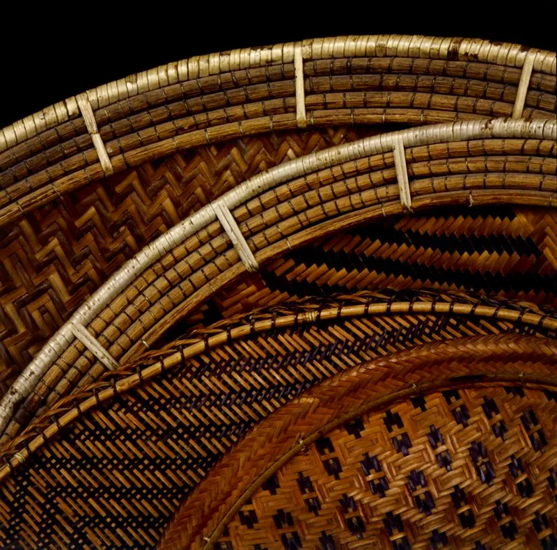 Detalle de diferentes tipos de balay en fibras e yarumo, fabricados por diversas comunidades indígenas del Amazonas y de los Llanos Orientales. La forma como entretejen la fibra y su coloración, al igual que el remate de los bordes, distinguen no sólo el uso dado a cada uno de ellos, sino a un grupo humano de otro. Son utilizados en el proceso de elaboración de la yuca brava. Tras su rallado, la pulpa se aprieta contra el balay colocado sobre un trípode. Luego se introduce en el sebucán para extraer el veneno. El producto resultante es un polvo blanco y harinoso que puede ser utilizado en dos formas: como casabe o como mañoco. José Fernando Machado