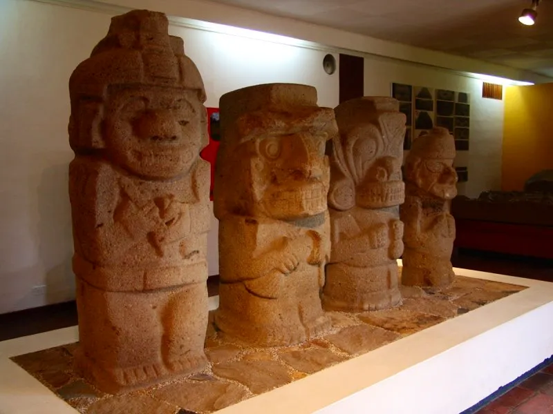 Cuatro personajes con distintos atributos en sus manos, tallados en bloque paralelepípedo. La estatua del extremo izquierdo procede de Uyumbe y las restantes de la Mesita B del Parque Arqueológico de San Agustín, y hoy se encuentran en el Museo de dicho Parque. En estos ejemplos puede percibirse el poder evocador que por sí sola tiene la forma de las piedras en la estatuaria del Macizo Colombiano. Independientemente de su tamaño, el bloque lítico produce sensaciones de fuerza, masa, gravedad, peso, poder, rasgos sin duda asociados con la imagen de la categoría de los chamanes representados aquí. La simple forma guarda un contenido y contribuye a transformar una imagen mental socialmente compartida —la del chamán— en imagen visual y artística plenamente comprensible.