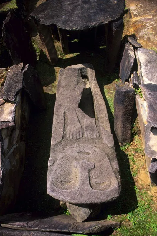 Tapa de sarcófago en el Montículo II de la Meseta A del Alto de los Ídolos, tallada en una técnica que combina el relieve tridimensional y el relieve biplano. La figura, representación masculina, no presenta las características fauces animales y sus ojos cerrados aluden sin duda a la muerte del personaje. La postura de las manos, un tanto rígida, responde al principio de frontalidad, frecuente en la estatuaria.