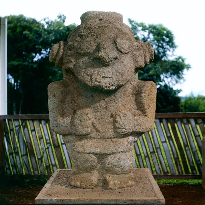 El estatismo de la estatuaria, consistente no solo en la falta de movimiento sino en el predominio del eje vertical, se ve atenuado por los objetos que portan los personajes, como la varita que lleva en la derecha esta figura de chamán procedente del Alto de los Ídolos, orientada de forma oblicua sobre el pecho. Las enormes orejeras tubulares acentúan el extraño aspecto del personaje.