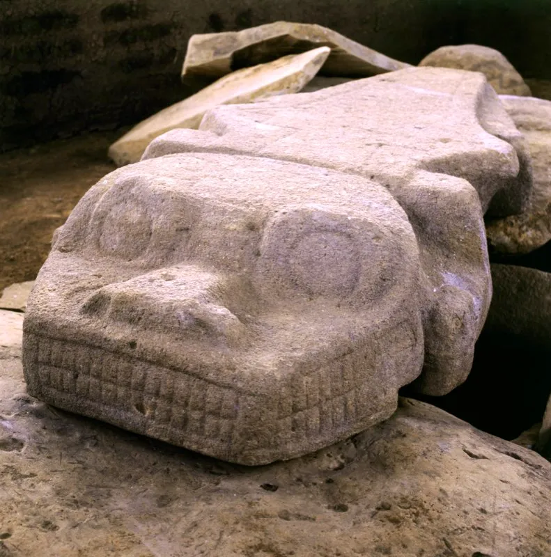 Figura labrada en una placa de más de dos metros de longitud, de la Meseta B del Alto de los Ídolos. Su cuerpo es el de un reptil, probablemente un caimán, pero su cabeza es la de un ser que combina características de mono y caimán. Los ojos y la nariz son del primero y las fauces del segundo, y de allí el extraordinario número de dientes que ostenta, el mayor de toda la estatuaria (14 incisivos por mandíbula).