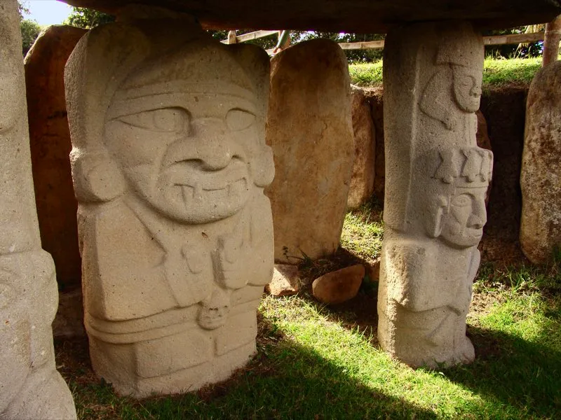 Alrededor de la mitad de las cerca de 300 estatuas que representan seres humanos —o seres más humanos que animales— en el arte del Macizo Colombiano responden a la definición de lo “hierático”, tanto en el sentido de que se relacionan con lo sagrado o sacerdotal, como en la solemnidad que las caracteriza. Como en el caso de esta estatua del Montículo Noroeste de la Mesita B del Parque Arqueológico de San Agustín, siguen fórmulas estilísticas estrictas, incluida la sujeción a las formas básicas de la piedra, el falo y la cruz. Lo más probable es que se trate de chamanes con distintos atributos (un cráneo trofeo en esta estatua), algunos ornamentos, fauces animales más o menos amenazadoras, nariz de mono platirrino y ojos que suelen guardar relación con alguna característica animal específica, como los ojos rasgados del jaguar en esta figura.