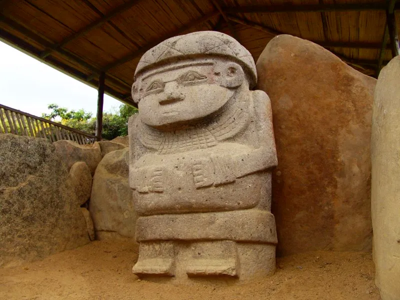 Figura de mujer hallada en el Alto de las Piedras. Se identifica como de género femenino no tanto por su voluminoso abdomen, que si bien podría ser señal de embarazo también indicaría simplemente obesidad, sino por la cinta sobre su frente, con decoración serpentina. Preuss observó en su mejilla izquierda un dibujo, quizás síntesis geométrica de la cabeza de un reptil, hoy totalmente borrado.