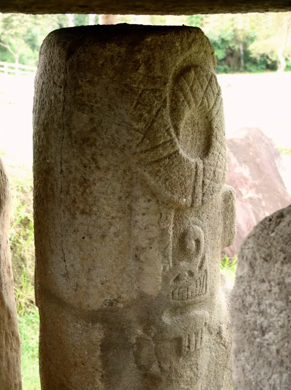 Los guerreros del Montículo Oriental de la Mesita A del Parque Arqueológico de San Agustín muestran una fase crucial en la metamorfosis del mono-serpiente. Por el frente, directamente sobre el rostro del guerrero, aparece su parte superior, con sus dos brazos, ojos cerrados de animal muerto, un penacho sobre la cabeza y, a diferencia de otras representaciones, con fauces animales. El cuerpo de la serpiente, decorado con franjas de círculos y motivos reticulares, parece dividirse en dos –efecto técnico común en el arte prehispánico para mostrar dos lados de un mismo animal-, para terminar, luego de enroscarse, en la cabeza de otro animal cuyas características fauces de afilados dientes, ojos realzados y hocico terminado en exagerada punta que forma una voluta, lo identifican claramente como un caimán con brazos y manos humanos.