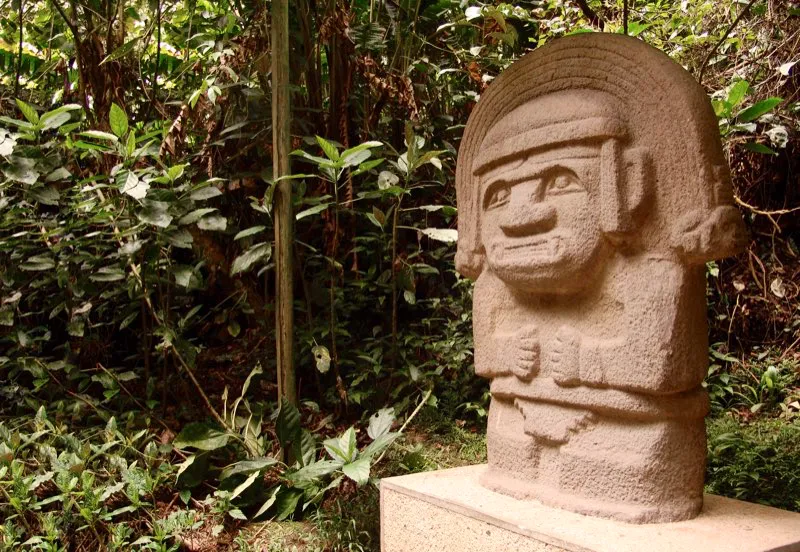 Esta extraordinaria estatua, originalmente en la Mesita C del Parque Arqueológico de San Agustín y hoy en el Bosque de las Estatuas, es una buena síntesis de la técnica escultórica y de los valores simbólicos y representativos de la estatuaria del Macizo Colombiano. Es figura masculina, por el taparrabos en forma de pirámide escalonada invertida, pero también puede describirse como femenina, por el cabello dividido en curvas dobles, y por lo tanto reúne los dos principios esenciales de la fertilidad, como los reúne el mono-serpiente de cabeza doble que forma su tocado. Tanto en términos físicos como metafóricos, está dotada de un halo singular que eleva objetos comunes de la vida cotidiana —el mono, la serpiente, el peinado, el vestido— a otros mundos y otras realidades; al mundo ultraterreno de la religión y al mundo del arte.