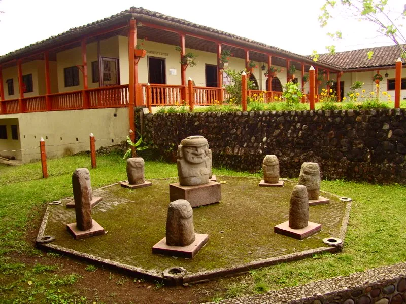 Grupo de las pequeñas esculturas columnarias conocidas como “guardianes de tumbas”, dispuestas en torno a una estatua hallada cerca al río Naranjos, en proximidades del Parque Arqueológico de San Agustín. Rescatadas por arqueólogos luego de servir algunas de ellas de soportes a columnas en los patios de las casas, son posiblemente la muestra más palmaria de nuestra moderna incomprensión del mundo del arte y el mundo de la vida en el Macizo Colombiano prehispánico. Probablemente jamás sirvieron de soporte, ni estuvieron expuestas a la vista, ni son ejemplos de “las esculturas más arcaicas”, como las vio José Pérez de Barradas en su expedición de 1937. Y seguramente tampoco estuvieron asociadas con la muerte sino con la vida, pues son la imagen del mono-serpiente, alegoría de la fertilidad en la estatuaria.